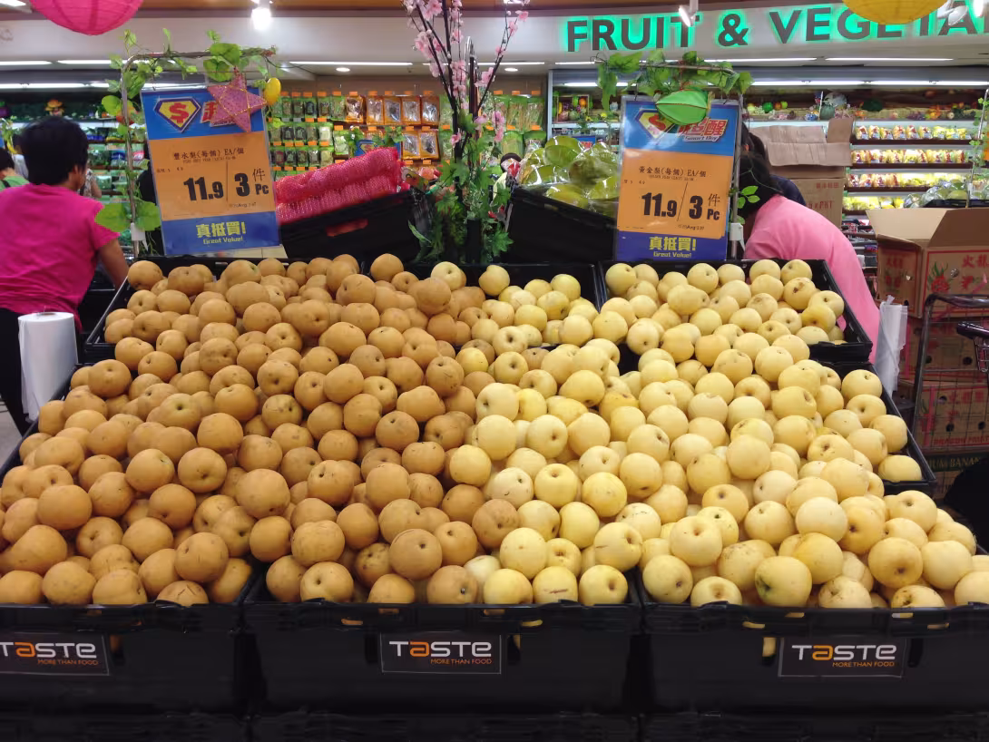 Lose gelbe und goldbraune asiatische Birnen in der Obstauslage eines Supermarkts in Hongkong, mit Preisschildern über den Früchten.